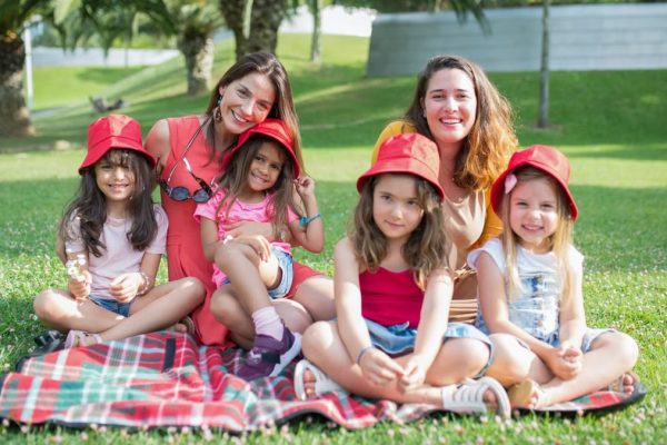 Friends enjoying a sunny day picnic on grass with bucket hats and smiles in a Portuguese park.