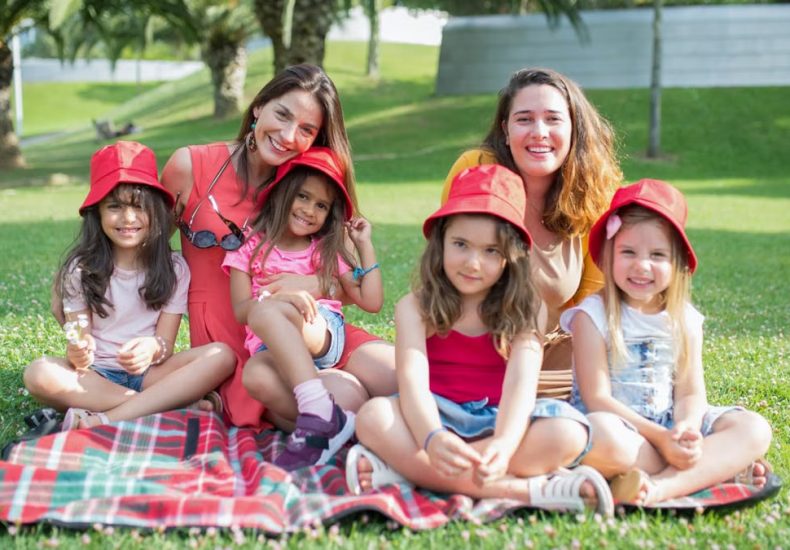 Friends enjoying a sunny day picnic on grass with bucket hats and smiles in a Portuguese park.